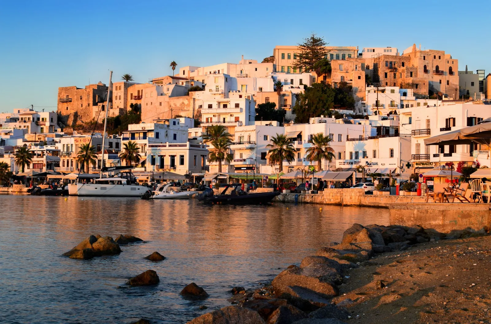 Naxos Town a jeho přístav v záři zlatého západu slunce, s budovami ozářenými do terakotova odstínu tyčícími se nad vodou